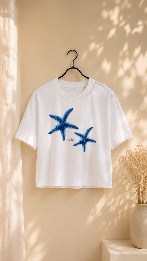 White t-shirt with blue starfish design on a hanger against a beige wall.